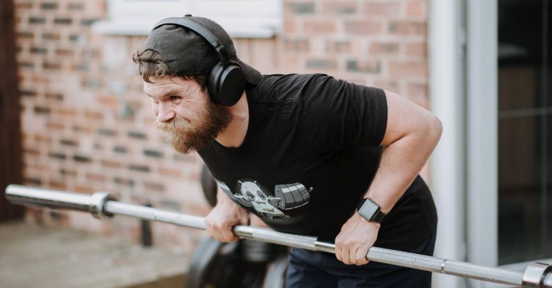 Brick Workouts - Brutal male with headphones pulling massive metal barbell on blurred background of brick house