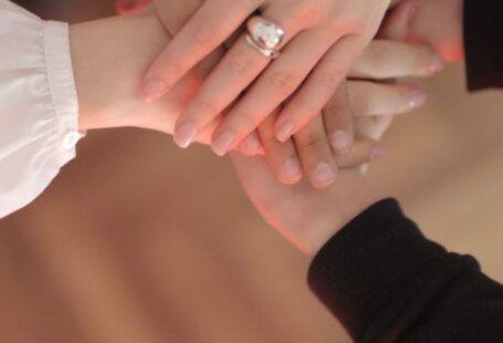 Equalizing Techniques - Top view of faceless friends in different clothes stacking hands together while standing on wooden floor indoor on sunny day