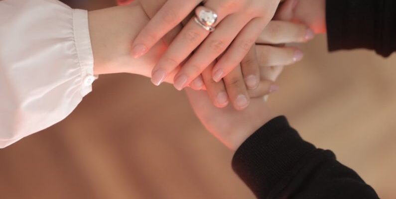 Equalizing Techniques - Top view of faceless friends in different clothes stacking hands together while standing on wooden floor indoor on sunny day