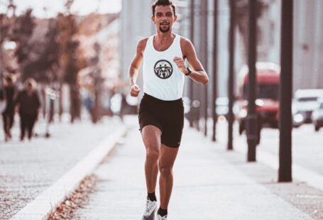 Interval Workouts - Full body of runner in sportswear jogging along paved pavement in sunny day in city