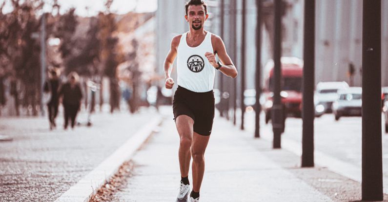 Interval Workouts - Full body of runner in sportswear jogging along paved pavement in sunny day in city