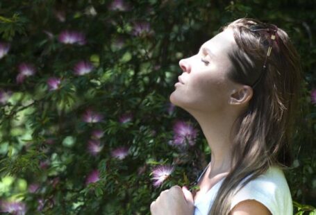 Breathing - Woman Closing Her Eyes Against Sun Light Standing Near Purple Petaled Flower Plant