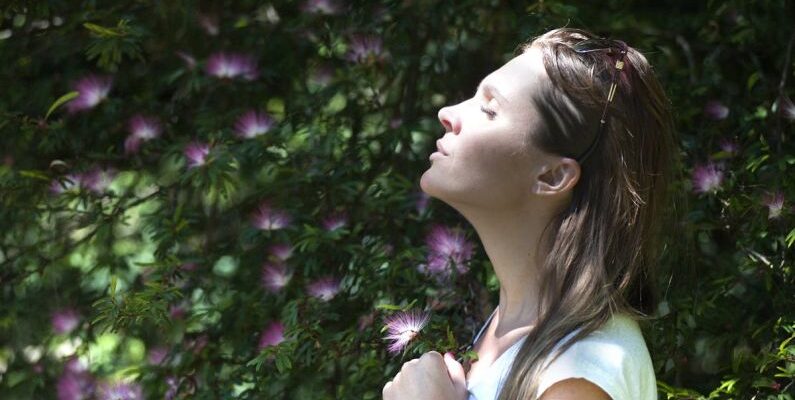 Breathing - Woman Closing Her Eyes Against Sun Light Standing Near Purple Petaled Flower Plant