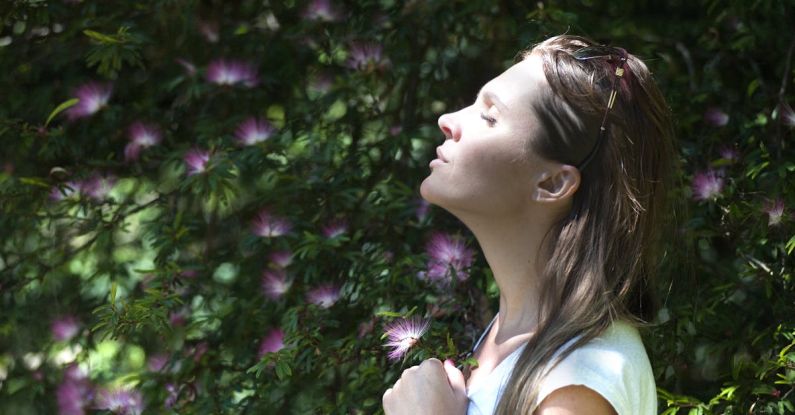 Breathing - Woman Closing Her Eyes Against Sun Light Standing Near Purple Petaled Flower Plant