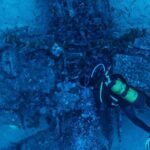 Dive Gear - Top view of unrecognizable person in wetsuit inspecting rough remains of sunken plane on bottom of sea