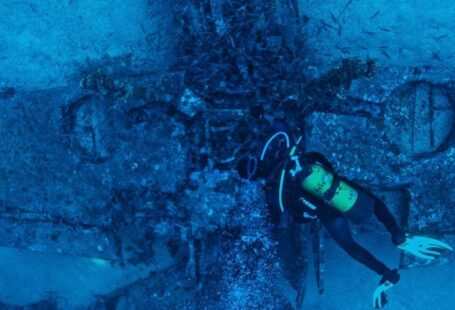 Dive Gear - Top view of unrecognizable person in wetsuit inspecting rough remains of sunken plane on bottom of sea