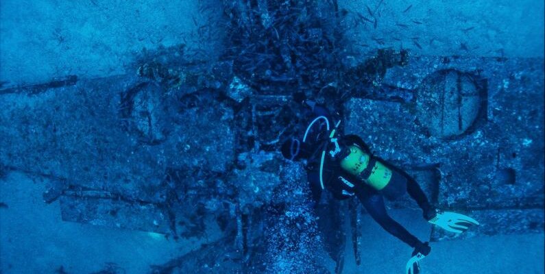 Dive Gear - Top view of unrecognizable person in wetsuit inspecting rough remains of sunken plane on bottom of sea