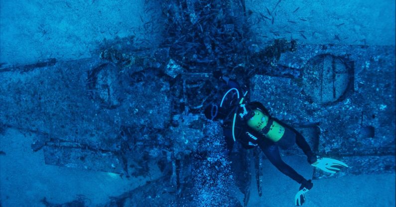 Dive Gear - Top view of unrecognizable person in wetsuit inspecting rough remains of sunken plane on bottom of sea