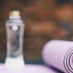 Aqua Yoga - Roll of violet yoga mat with transparent plastic bottle of water on blurred background