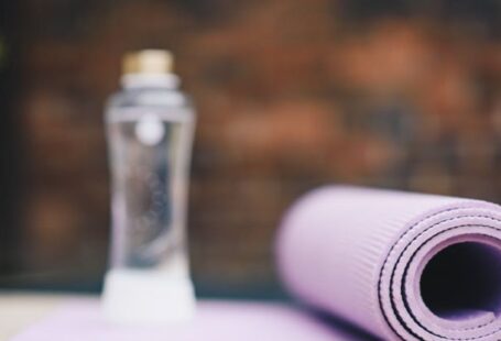 Aqua Yoga - Roll of violet yoga mat with transparent plastic bottle of water on blurred background