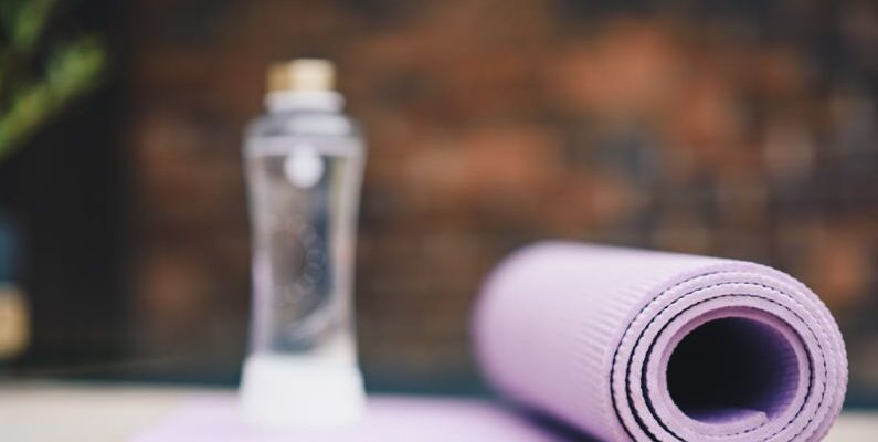 Aqua Yoga - Roll of violet yoga mat with transparent plastic bottle of water on blurred background