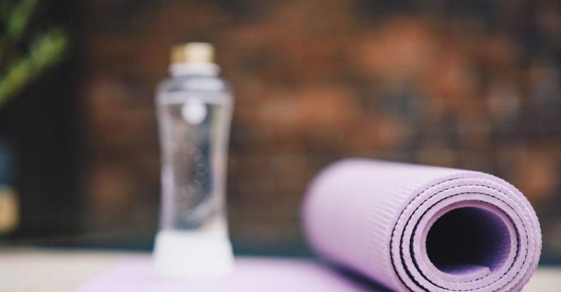 Aqua Yoga - Roll of violet yoga mat with transparent plastic bottle of water on blurred background