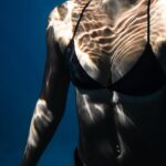 Dive Techniques - Underwater shot of fit young female in black bikini swimming in dark blue seawater with eyes closed