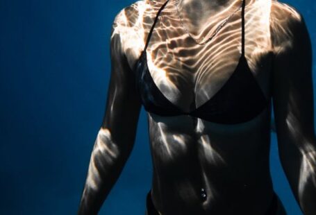 Dive Techniques - Underwater shot of fit young female in black bikini swimming in dark blue seawater with eyes closed