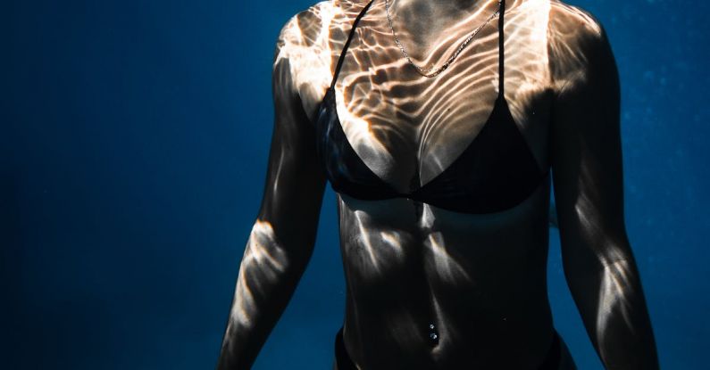 Dive Techniques - Underwater shot of fit young female in black bikini swimming in dark blue seawater with eyes closed